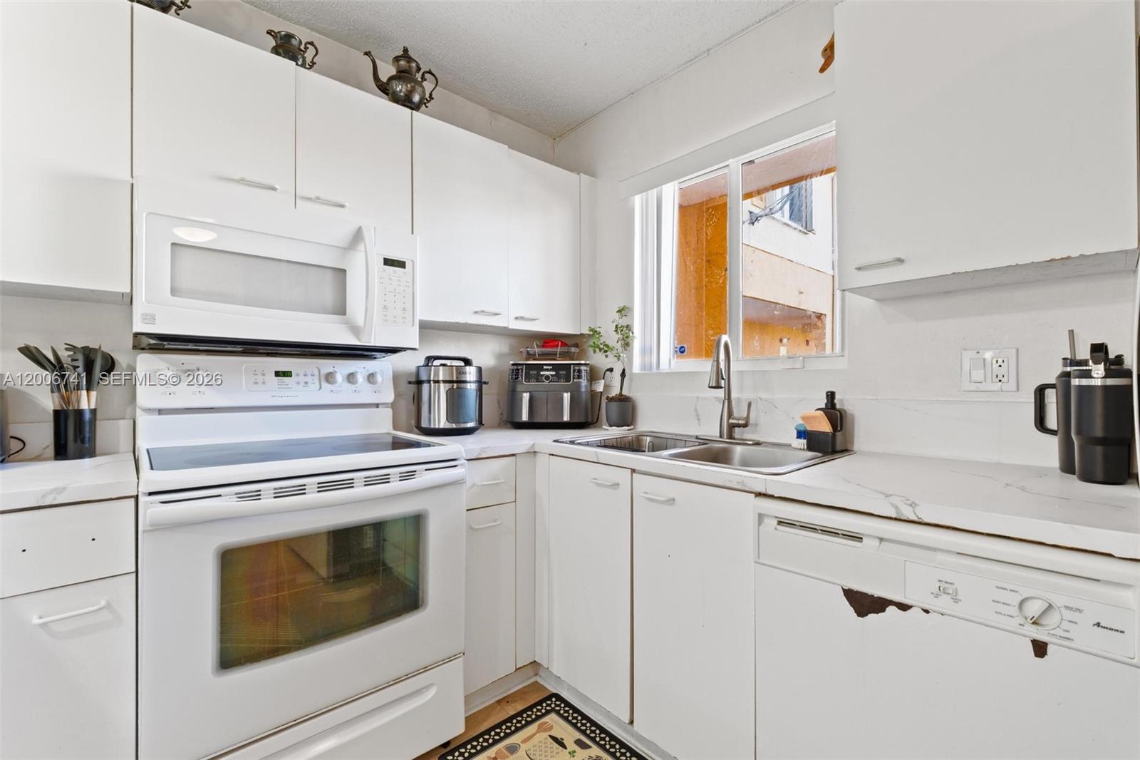 A white kitchen features a stove, microwave, sink, and dishwasher with white cabinetry and countertops — 6235 Kendale Lakes Cir # 247, Miami FL 33183, MIAMI, FL