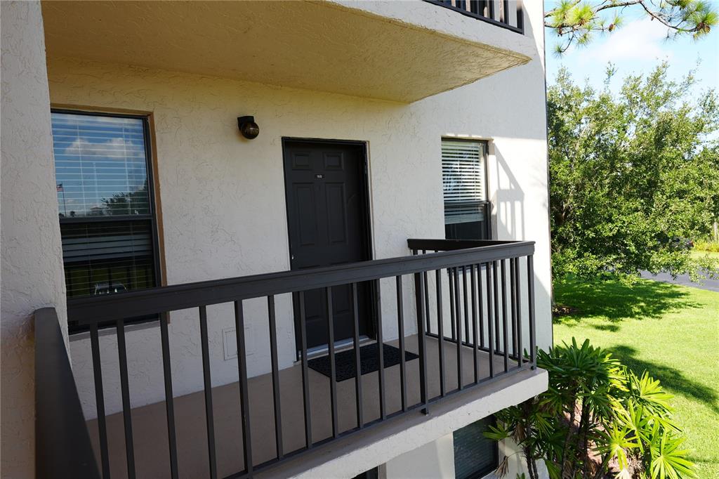 An exterior view of an apartment balcony with a dark door and metal railing — 1999 KINGS HIGHWAY UNIT 16B, PUNTA GORDA, FL