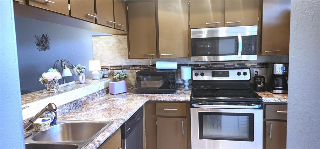 A kitchen features brown cabinets, stainless steel appliances, and a patterned laminate countertop — 1999 KINGS HIGHWAY UNIT 16B, PUNTA GORDA, FL