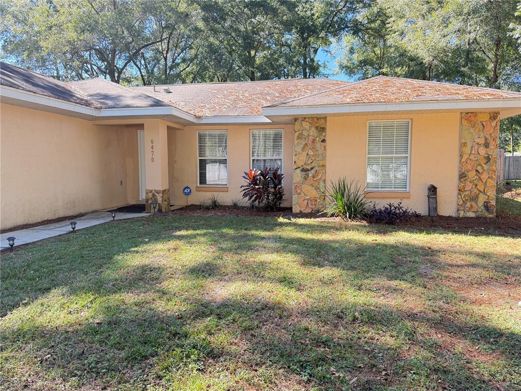 A single-story house with a tan stucco exterior, stone accents, and a shingled roof — 6470 NW 56TH TERRACE, OCALA, FL