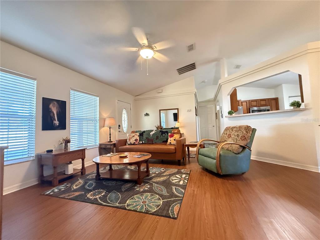A living room features wood-look flooring, a brown sofa, a green armchair, and a ceiling fan — 6470 NW 56TH TERRACE, OCALA, FL