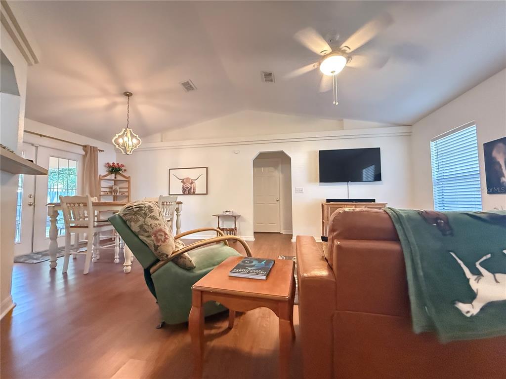 A living room with vaulted ceilings, wood-look flooring, a ceiling fan, and a dining area — 6470 NW 56TH TERRACE, OCALA, FL