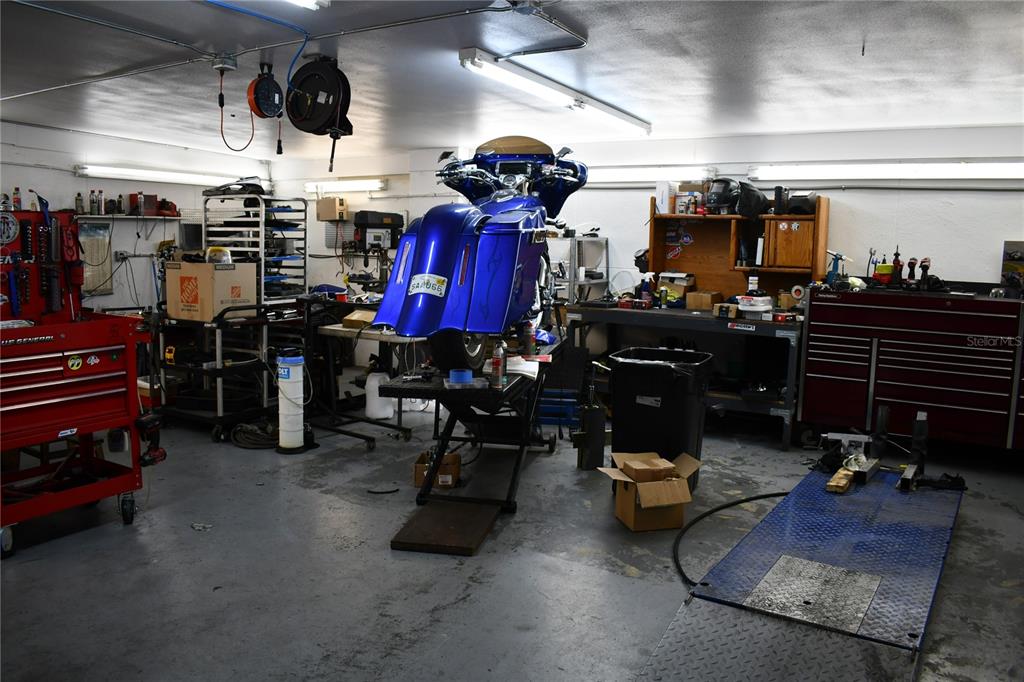 A garage workshop features a blue motorcycle on a lift, tool chests, and workbenches — 2702 E 7TH AVENUE, TAMPA, FL