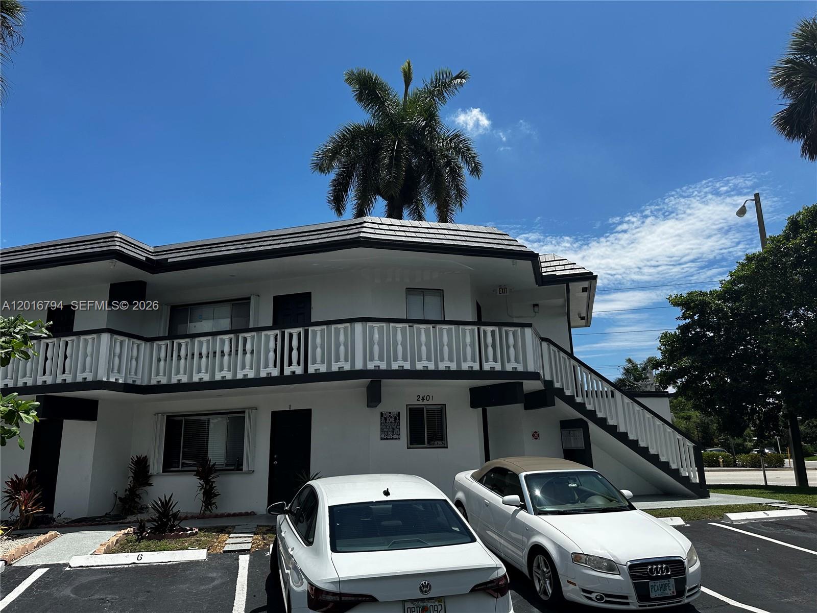 A two-story white apartment building features a balcony, exterior staircase, and a parking lot — 2401 NW 9th Ave # 8, Wilton Manors FL 33311, WILTON MANORS, FL