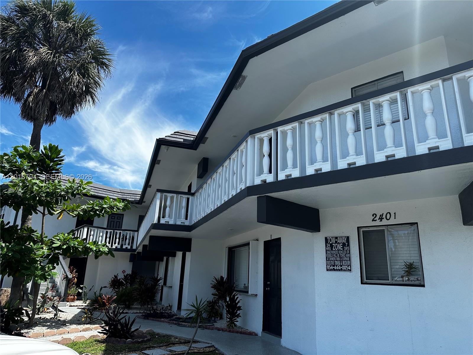 A two-story white apartment building features a balcony with white balusters and dark trim — 2401 NW 9th Ave # 8, Wilton Manors FL 33311, WILTON MANORS, FL