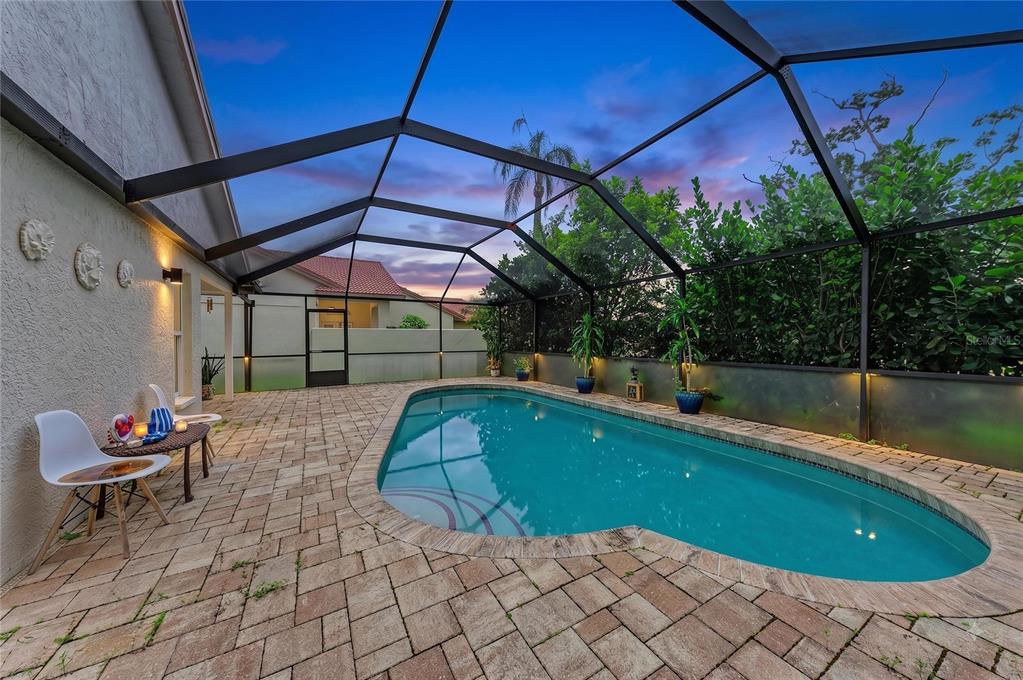 A screened-in patio features a kidney-shaped swimming pool surrounded by stone pavers at dusk — 4907 KILTY COURT E, BRADENTON, FL