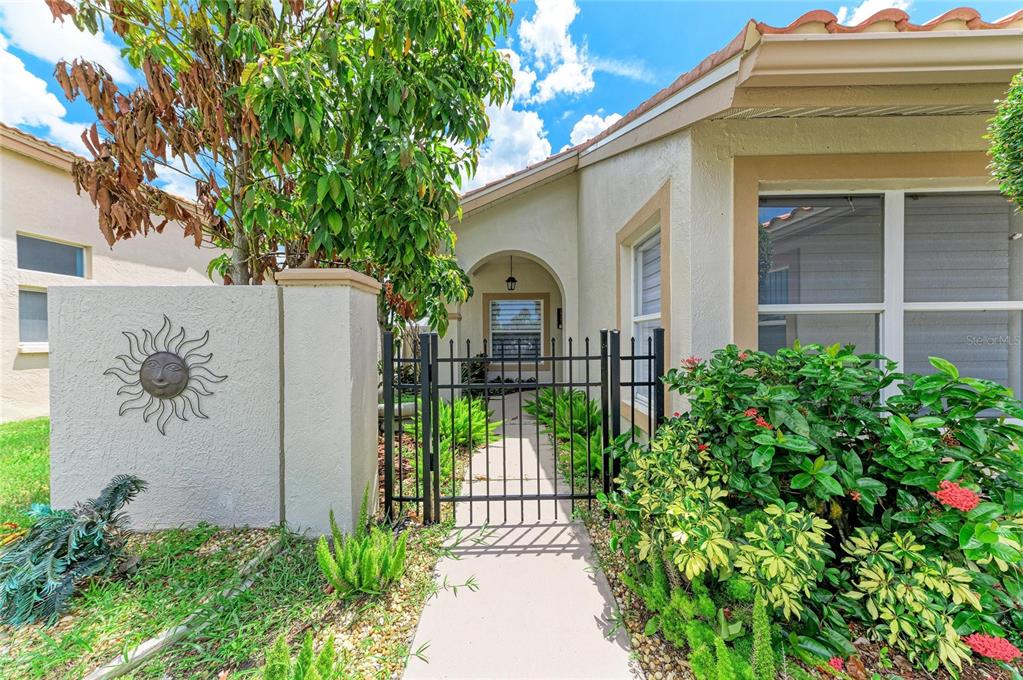 A gated walkway leads to the front entrance of a house with a sun wall decoration — 4907 KILTY COURT E, BRADENTON, FL
