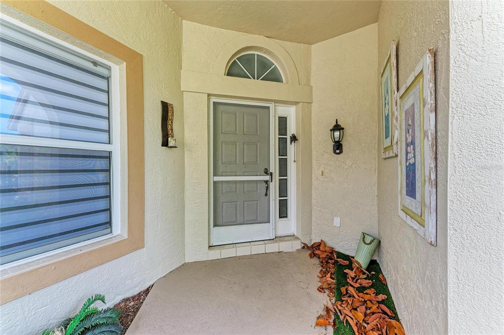 A covered entryway features a front door with a screen, a window, and wall decor — 4907 KILTY COURT E, BRADENTON, FL