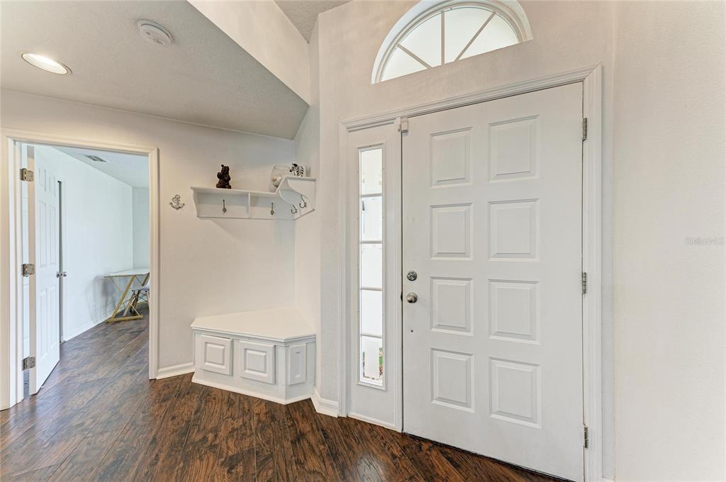 An entryway features a white front door, a built-in bench, and dark wood-look flooring — 4907 KILTY COURT E, BRADENTON, FL