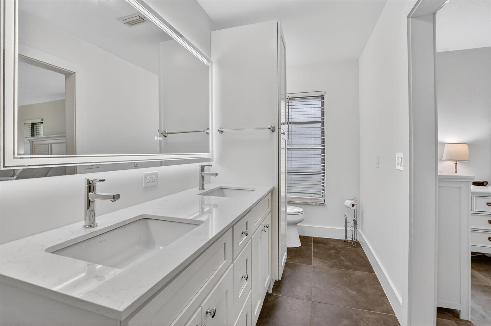 A bathroom features a double vanity with white cabinets, quartz countertops, and dark tile flooring — 3693 Arelia Drive N, Delray Beach FL 33445, DELRAY BEACH, FL