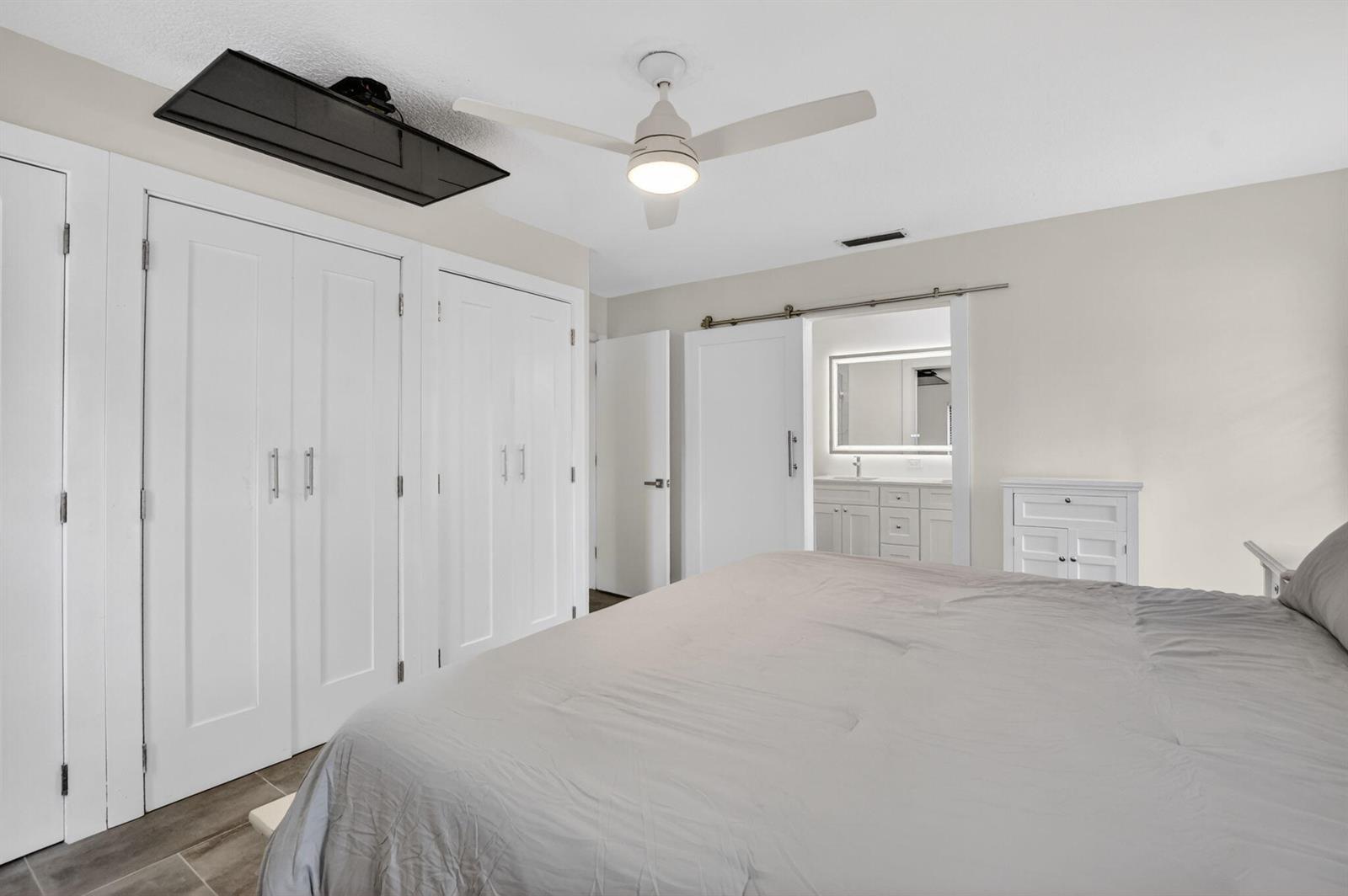 A bedroom features a bed, white closet doors, a ceiling fan, and a sliding barn door — 3693 Arelia Drive N, Delray Beach FL 33445, DELRAY BEACH, FL