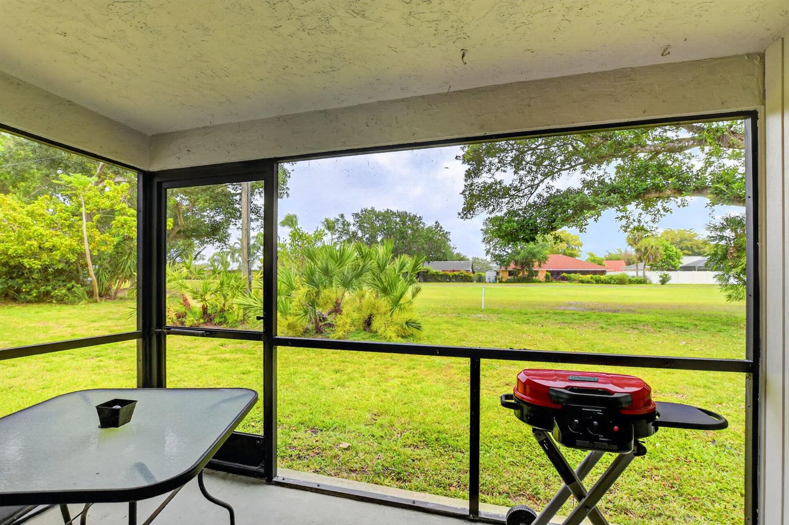 A screened-in porch overlooks a grassy backyard with trees and a distant house — 3693 Arelia Drive N, Delray Beach FL 33445, DELRAY BEACH, FL