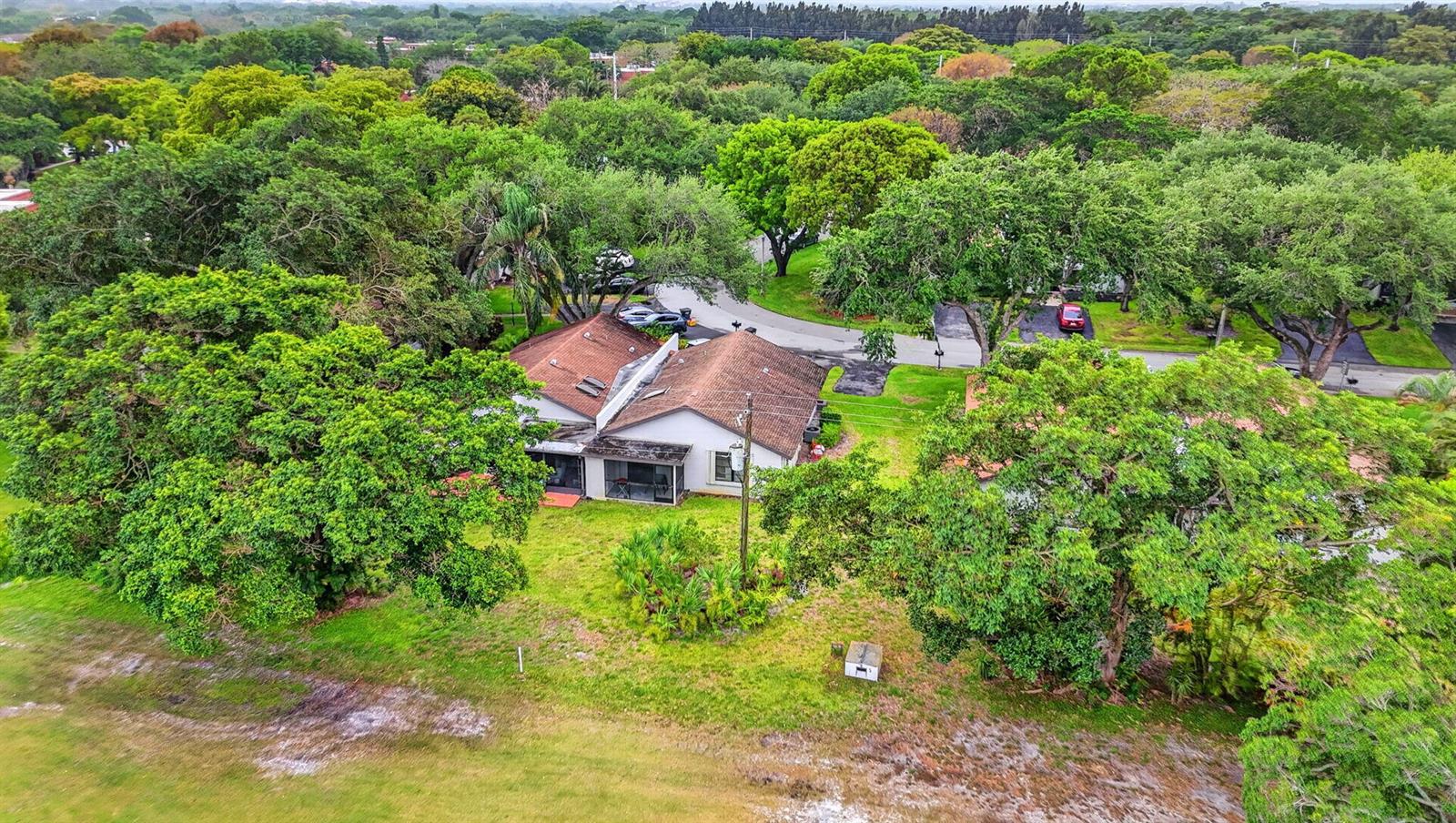 An aerial view shows a single-story house with a brown roof surrounded by lush trees — 3693 Arelia Drive N, Delray Beach FL 33445, DELRAY BEACH, FL