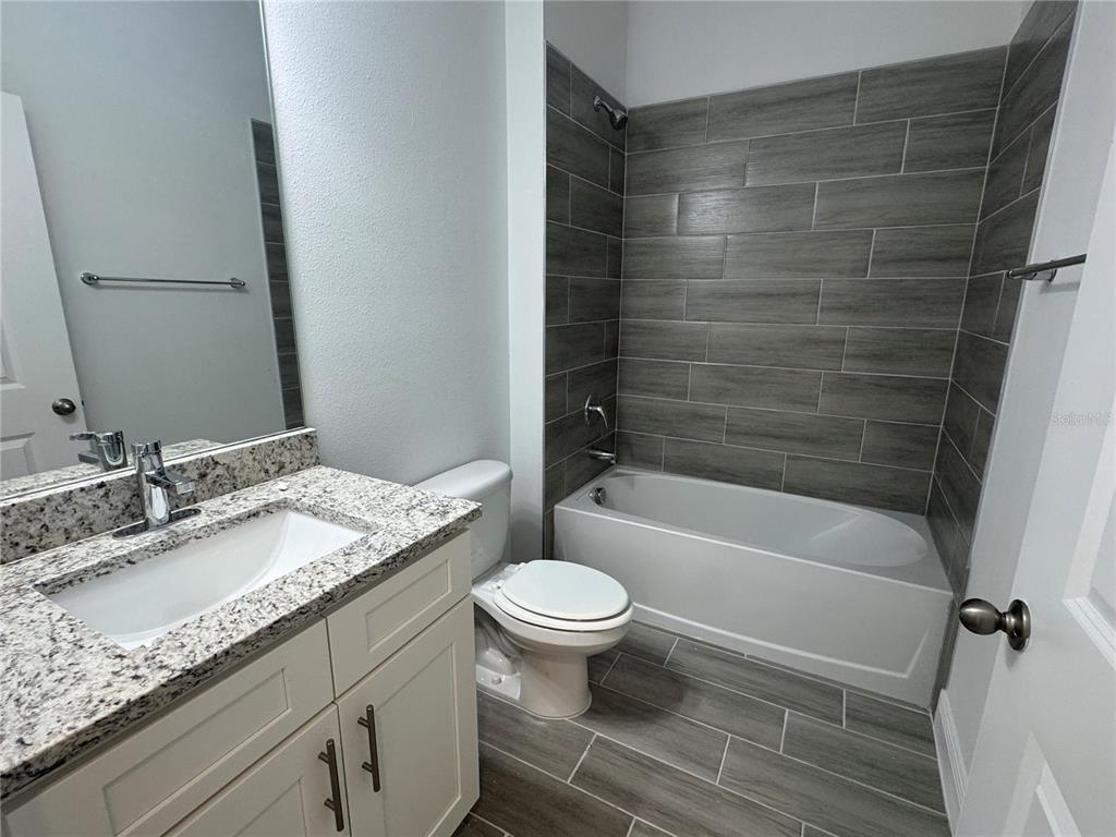 A bathroom features a granite vanity, white cabinets, a toilet, and a gray-tiled tub surround — 1602 CUMIN DRIVE UNIT 1602, POINCIANA, FL