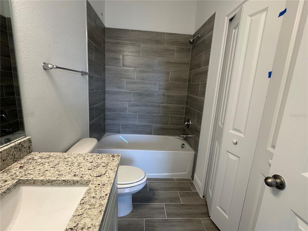 A bathroom features a granite vanity, a white toilet, and a tub with wood-look tile — 1602 CUMIN DRIVE UNIT 1602, POINCIANA, FL