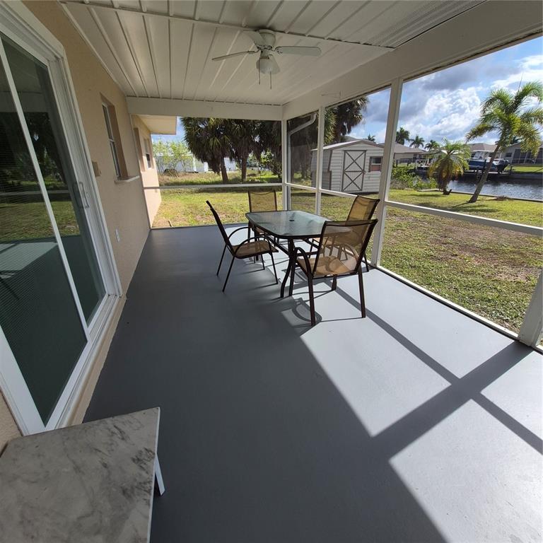 A screened-in patio features a gray floor, a dining set, and views of a canal — 5290 NEVILLE TERRACE, PORT CHARLOTTE, FL
