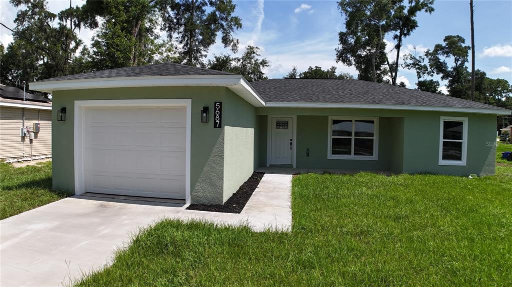 A single-story house with light green stucco siding, a white garage door, and a walkway — 5687 NW 57TH STREET, OCALA, FL