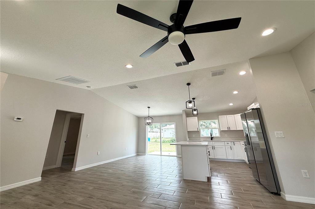 An open-concept kitchen and living area features white cabinets, a center island, and wood-look flooring — 5687 NW 57TH STREET, OCALA, FL