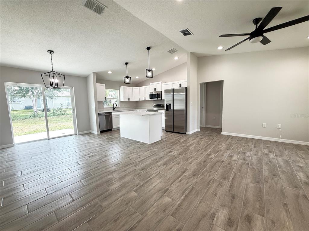 An open-concept kitchen and living area featuring white cabinets, a center island, and wood-look flooring — 5687 NW 57TH STREET, OCALA, FL