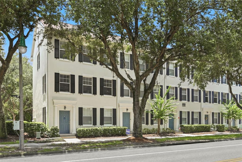 A row of three-story townhomes with white stucco walls and black shutters under large trees — 1020 WATERSIDE DRIVE UNIT 1020, CELEBRATION, FL
