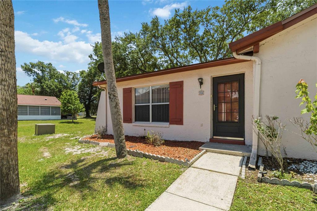 The exterior of a single-story house features a concrete walkway, red shutters, and a tree — 74 S MARBRISA WAY, KISSIMMEE, FL