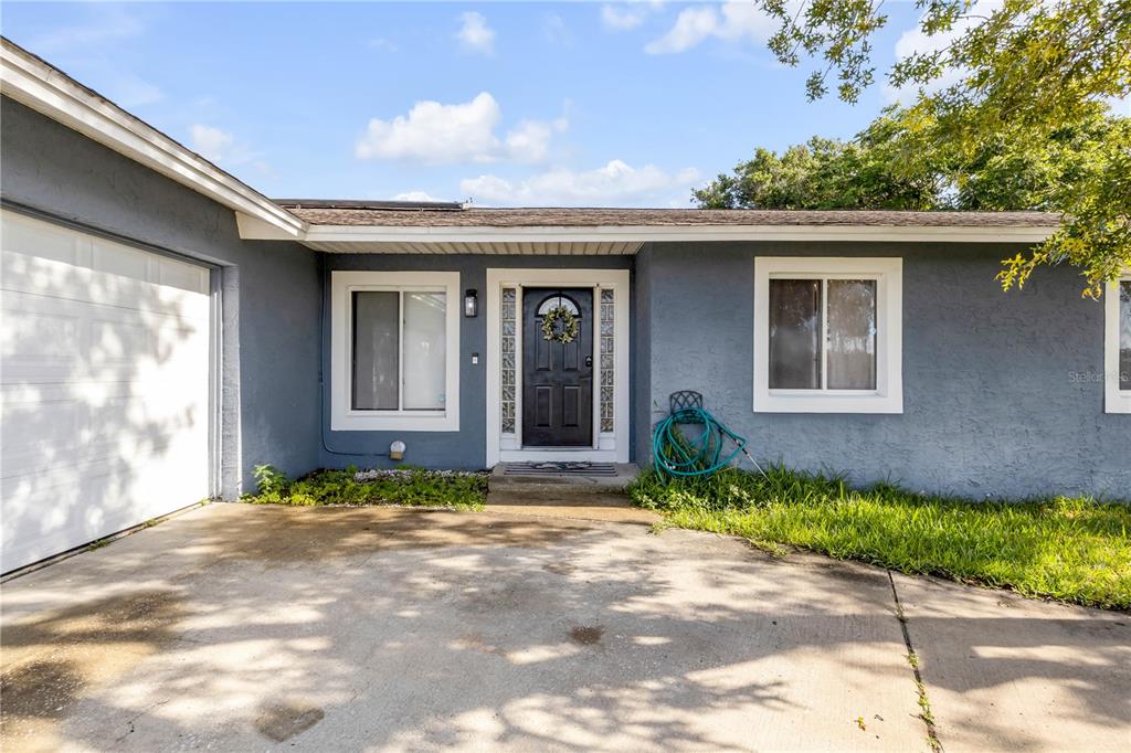 A gray single-story house features a white garage door, a black front door, and windows — 2550 VESPERO STREET, DELTONA, FL
