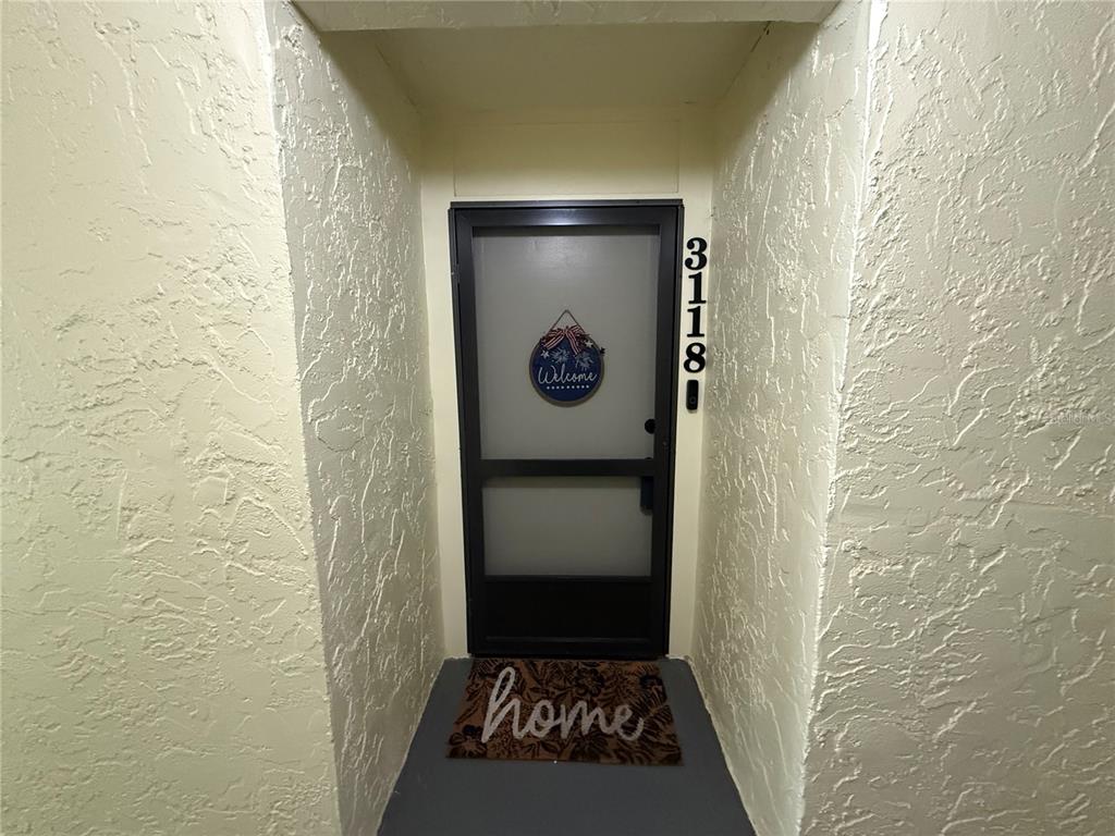 A front entryway features a screen door with a welcome sign and a home doormat — 14130 ROSEMARY LANE UNIT 3118, LARGO, FL