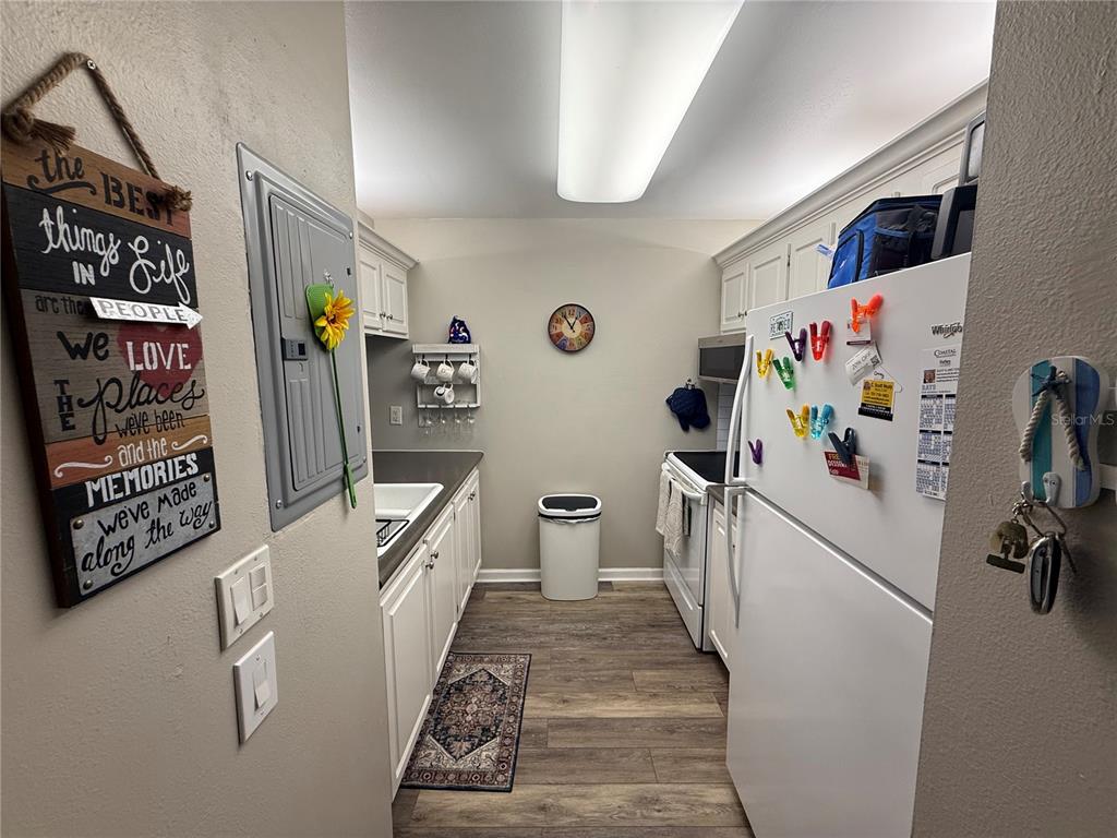 A galley-style kitchen features white cabinets, stainless steel appliances, and wood-look flooring — 14130 ROSEMARY LANE UNIT 3118, LARGO, FL