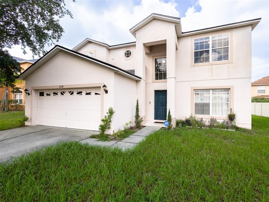 A two-story house with a beige stucco exterior, a two-car garage, and a front lawn — 2238 RIO GRANDE CANYON LOOP, POINCIANA, FL