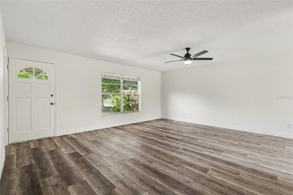 An empty living room features white walls, a ceiling fan, and gray wood-look flooring — 1916 HUDSON COURT, OLDSMAR, FL