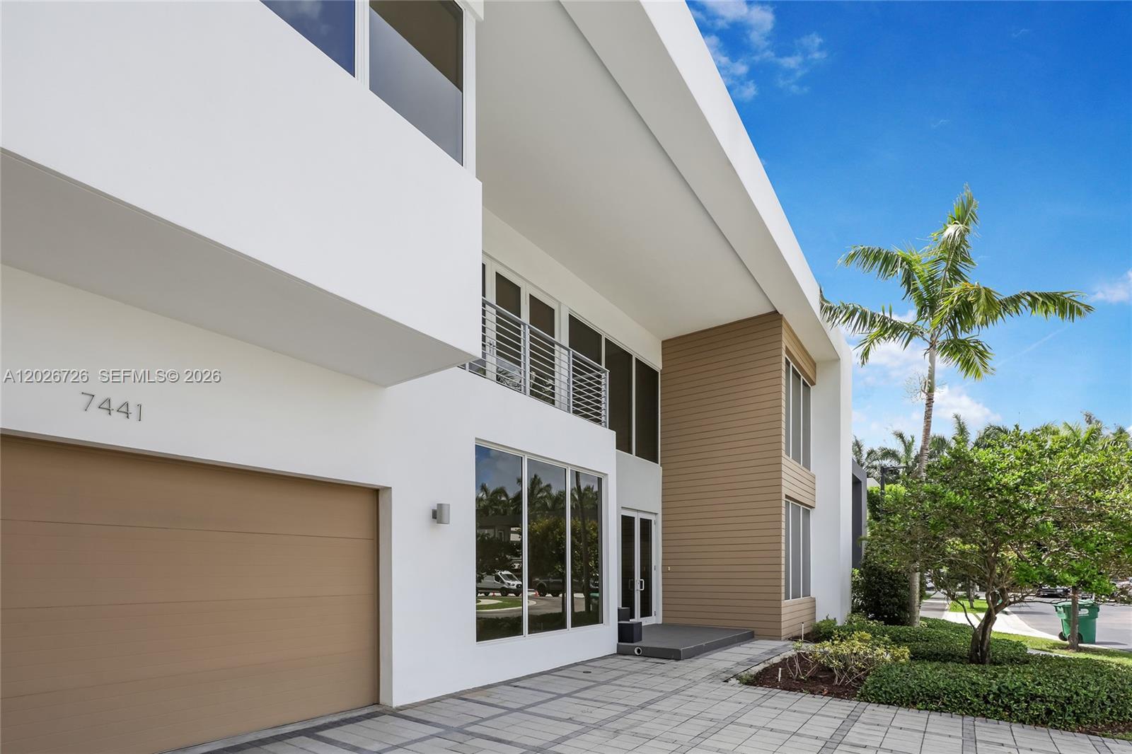 A modern two-story house features a white facade, wood-paneled accents, and a paved driveway — 7441 NW 102nd Ct, Doral FL 33178, DORAL, FL