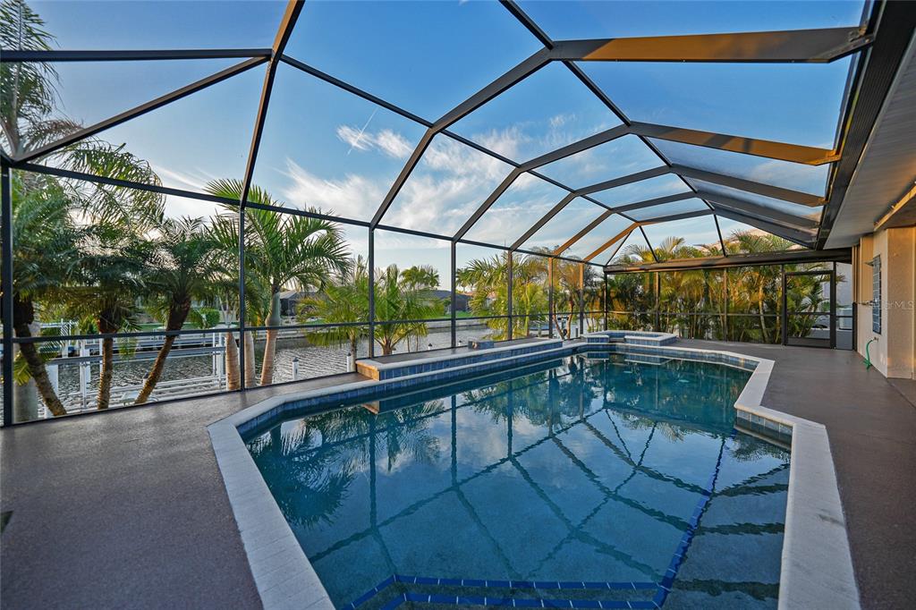 A screened-in pool area overlooks a canal with palm trees in the background — 718 ANTALYA COURT, PUNTA GORDA, FL