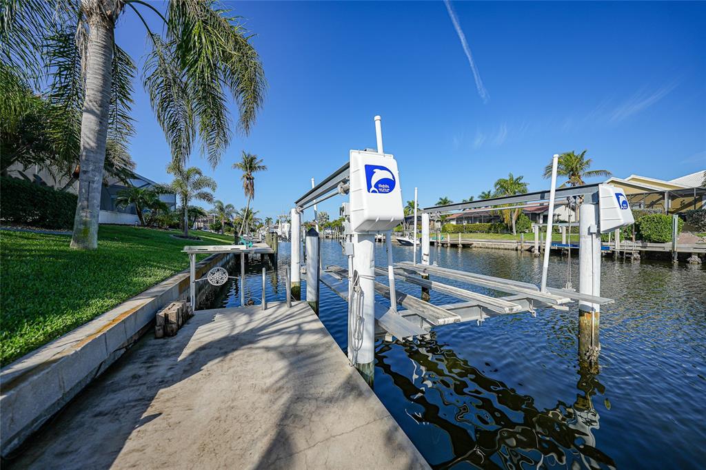 A concrete dock features a boat lift over a canal lined with palm trees — 718 ANTALYA COURT, PUNTA GORDA, FL