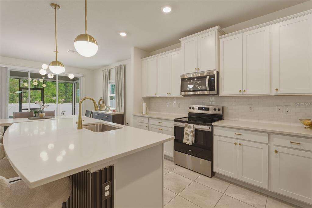 A modern kitchen features white cabinets, a large quartz island with a sink, and stainless appliances — 17664 NW 173RD ROAD, ALACHUA, FL