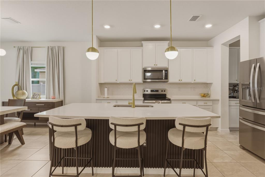 A modern kitchen features white cabinetry, a large dark-paneled island with seating, and gold fixtures — 17664 NW 173RD ROAD, ALACHUA, FL