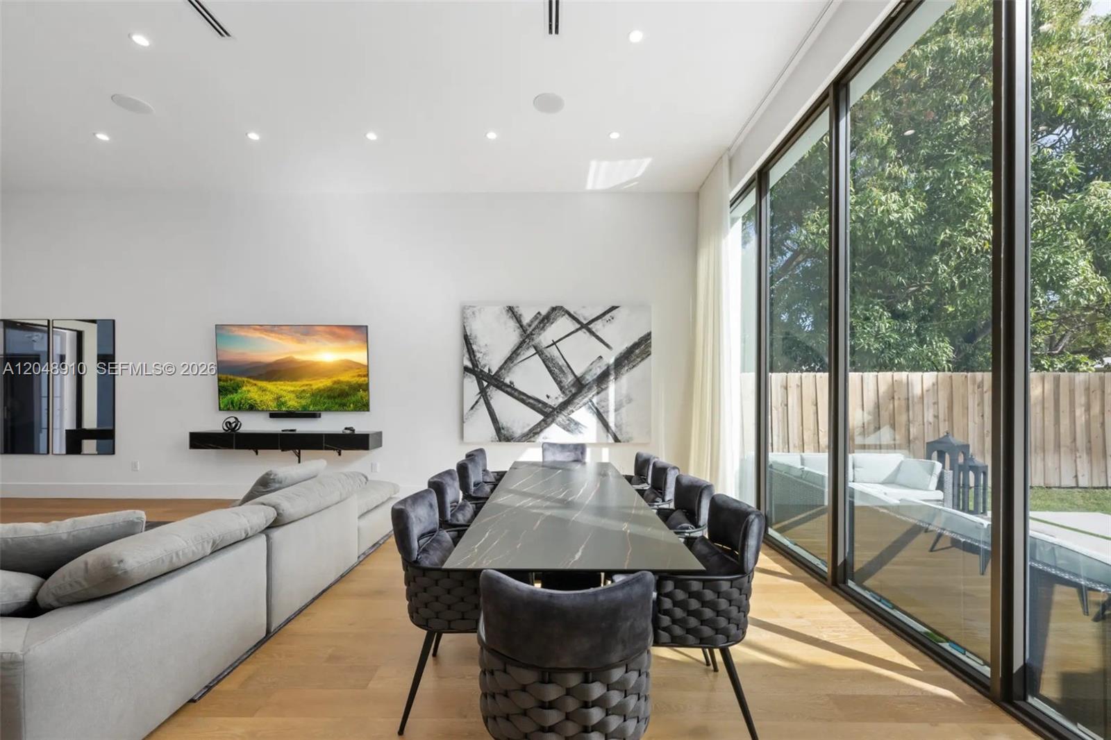 A modern dining and living area features a long marble table, grey chairs, and floor-to-ceiling windows — 80 NW 45th St, Miami FL 33127, MIAMI, FL