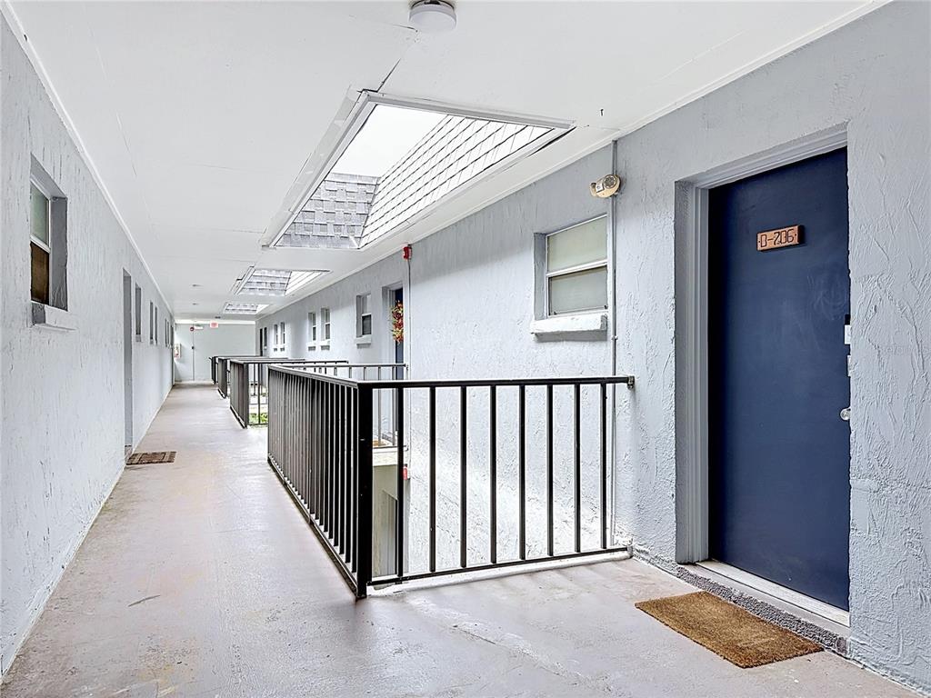 An outdoor apartment hallway features gray walls, a dark blue door, and skylights above — 5507 FOUNTAIN LAKE CIRCLE UNIT B206, BRADENTON, FL
