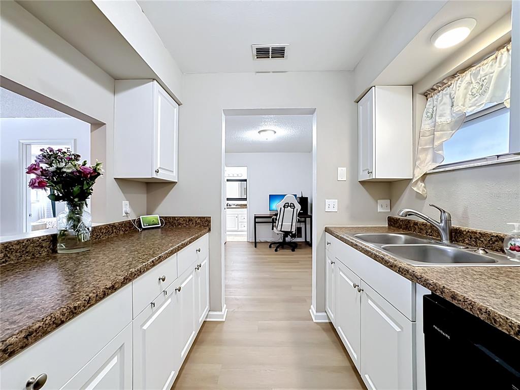 A galley kitchen features white cabinets, brown countertops, and a view into an adjacent office — 5507 FOUNTAIN LAKE CIRCLE UNIT B206, BRADENTON, FL