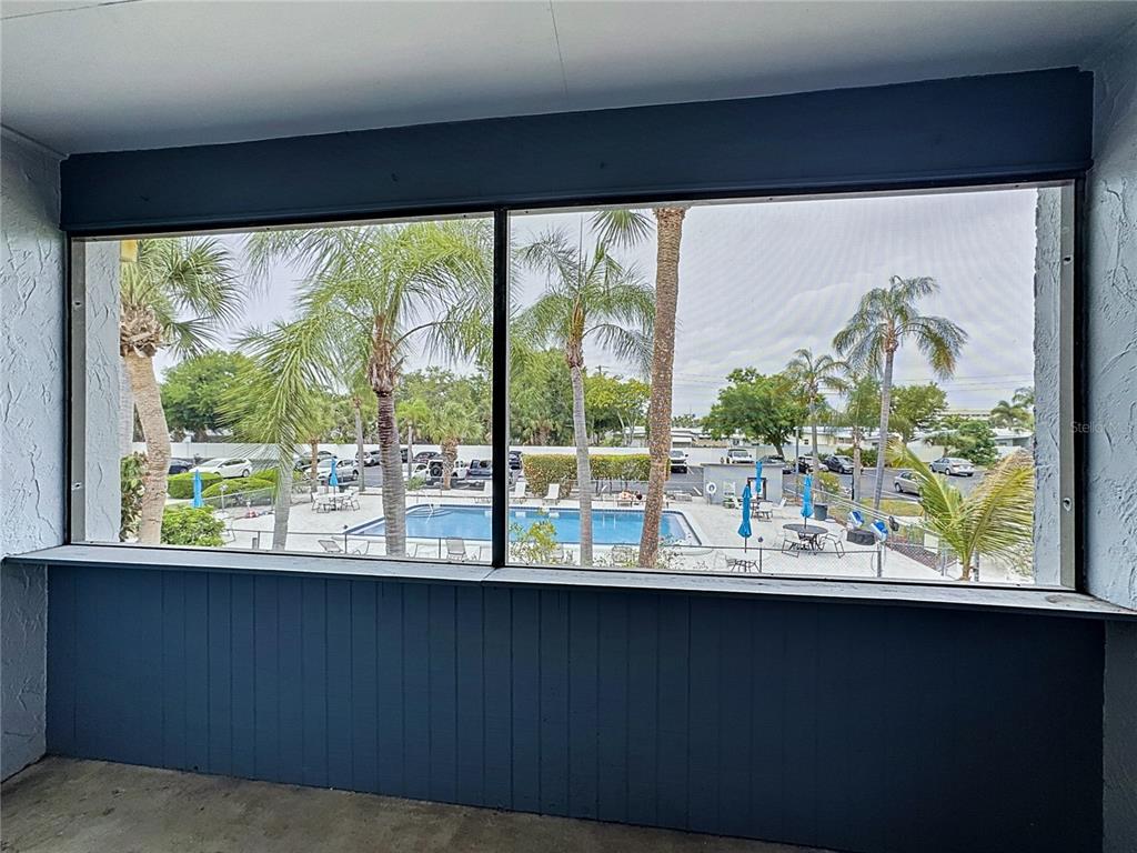 A screened-in porch overlooks a swimming pool and a parking lot with palm trees — 5507 FOUNTAIN LAKE CIRCLE UNIT B206, BRADENTON, FL