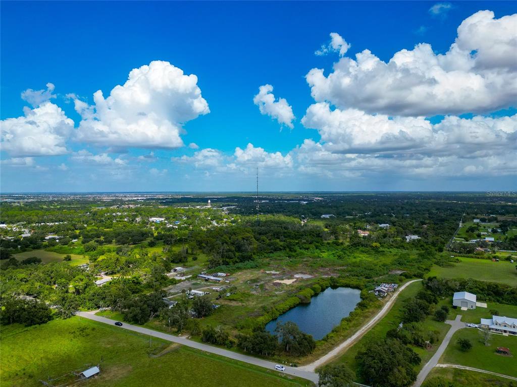 An aerial view shows a rural landscape with a pond, scattered buildings, and a radio tower — 301 EAST ROAD, SARASOTA, FL