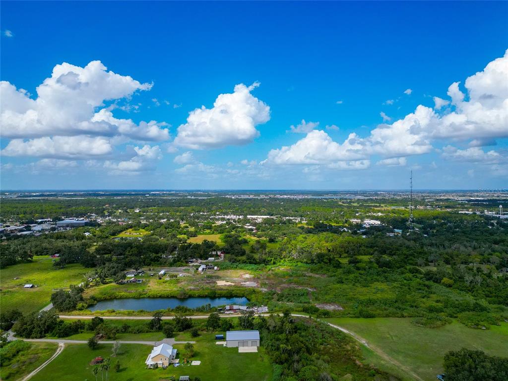 An aerial view shows a rural landscape with a pond, scattered buildings, and distant development — 301 EAST ROAD, SARASOTA, FL