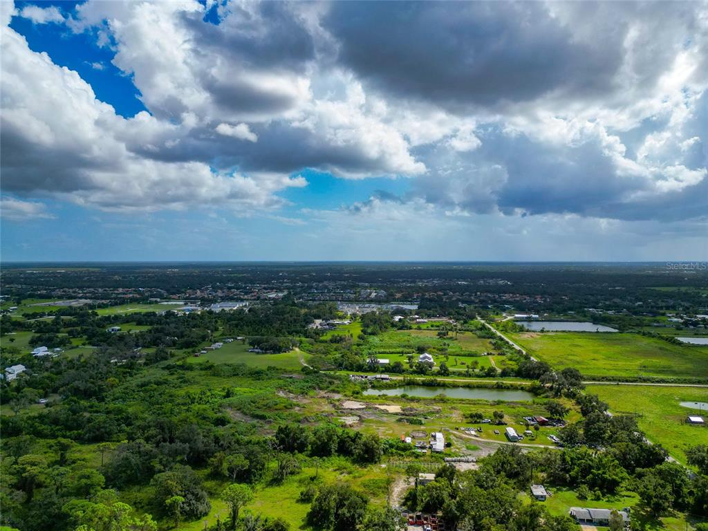 An aerial view shows a rural landscape with green fields, scattered trees, and small ponds — 301 EAST ROAD, SARASOTA, FL