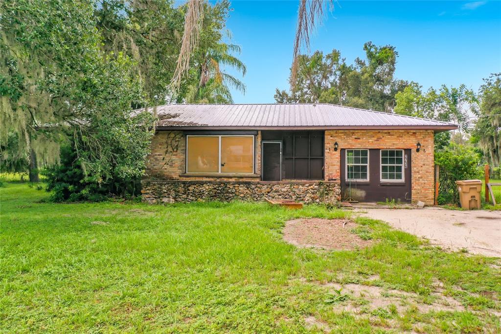 A single-story brick house with a metal roof and a stone-faced foundation sits outdoors — 2736 EMPIRE CHURCH ROAD, GROVELAND, FL
