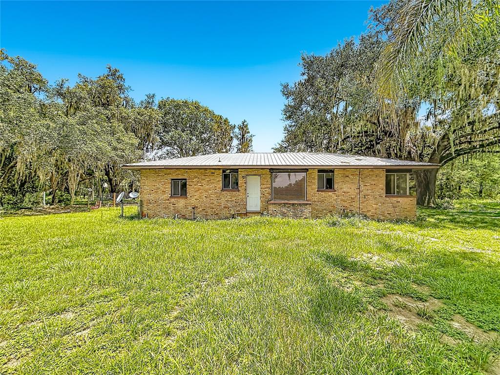 A single-story brick house with a metal roof sits in a grassy, tree-filled yard — 2736 EMPIRE CHURCH ROAD, GROVELAND, FL
