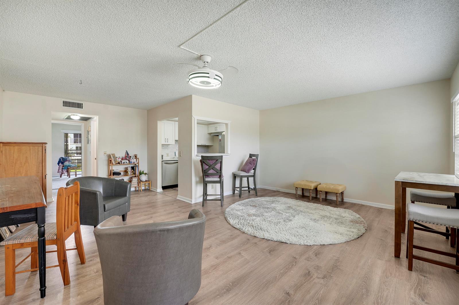 A living and dining area with light wood flooring, a ceiling fan, and neutral walls — 16 Mansfield A, Boca Raton FL 33434, BOCA RATON, FL