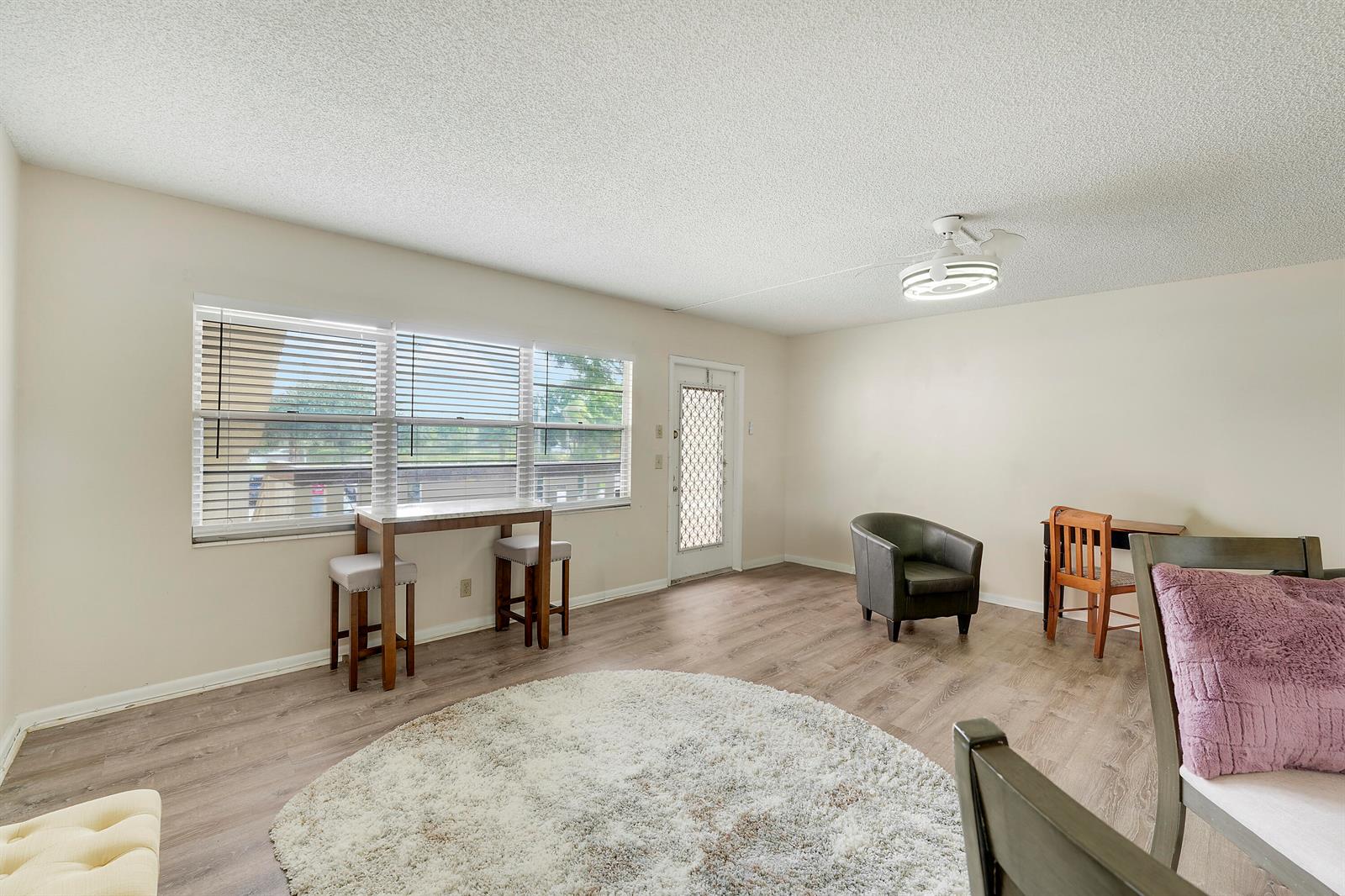 A living room with wood-look flooring, a white area rug, and a small dining table — 16 Mansfield A, Boca Raton FL 33434, BOCA RATON, FL