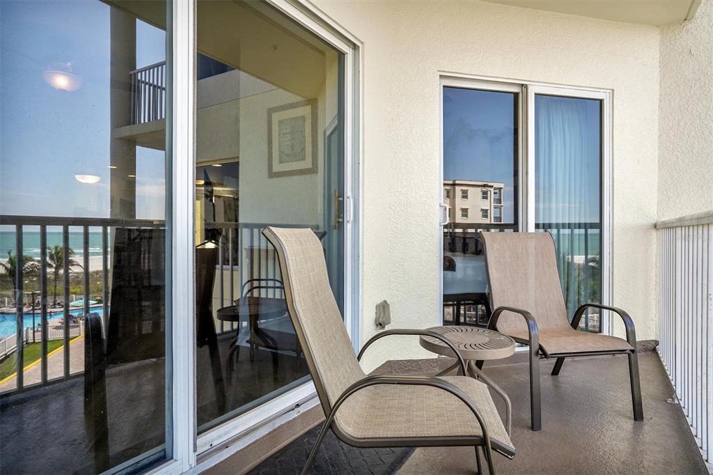 A balcony with two chairs and a small table overlooks a beach and pool area — 12000 GULF BOULEVARD UNIT 309N, TREASURE ISLAND, FL