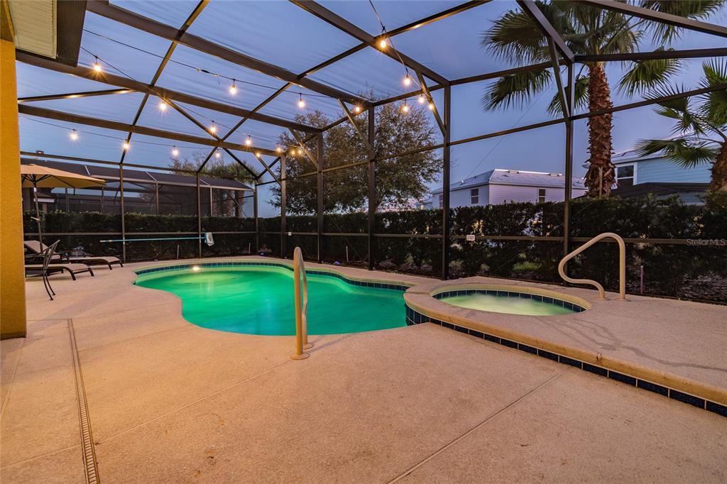A screened-in patio features a swimming pool, a spa, and string lights at dusk — 5352 OAKBOURNE AVENUE, DAVENPORT, FL