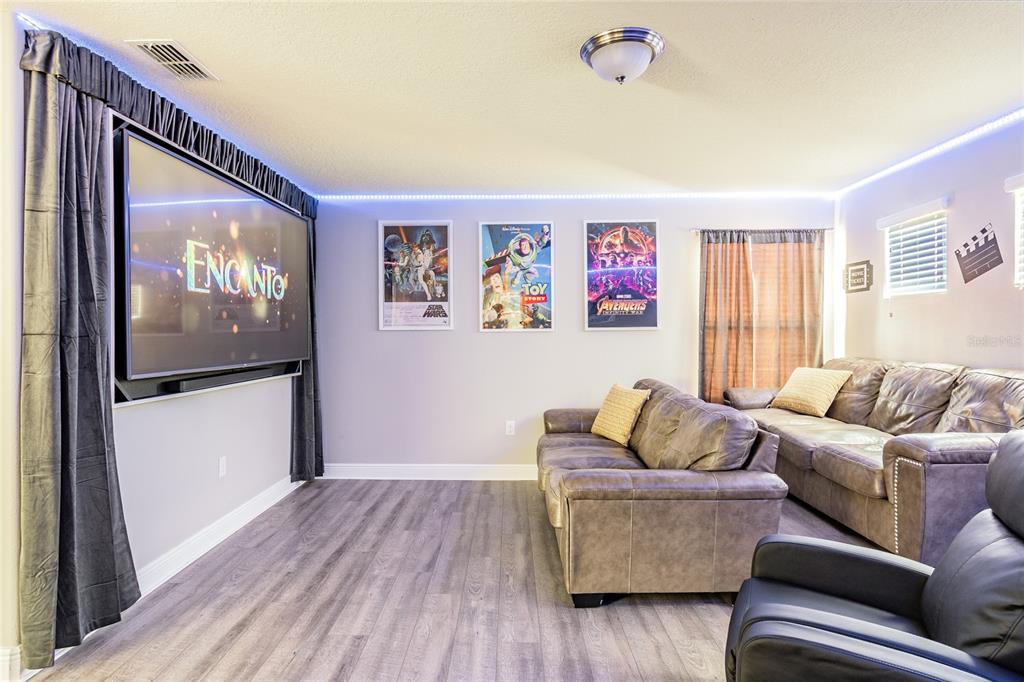 A home theater room features a large television, gray leather sofas, and movie posters — 5352 OAKBOURNE AVENUE, DAVENPORT, FL