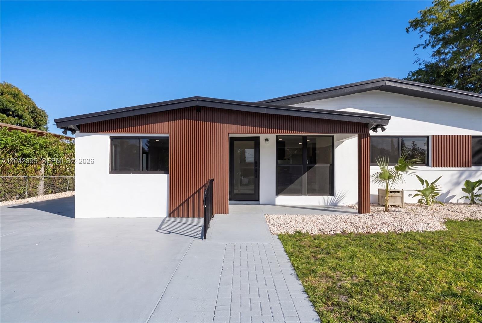 A single-story house features white stucco walls, a brown vertical-slat entryway, and a concrete driveway — 12471 SW 190th Ter, Miami FL 33177, MIAMI, FL